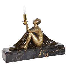 a bronze figurine holding a candle on top of a black marble base with gold accents