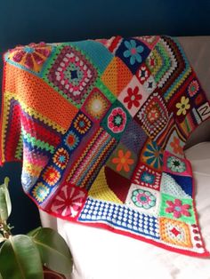 a colorful crocheted blanket sitting on top of a bed next to a potted plant