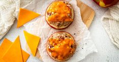 three baked apples with cheese on top and an apple next to them, sitting on parchment paper