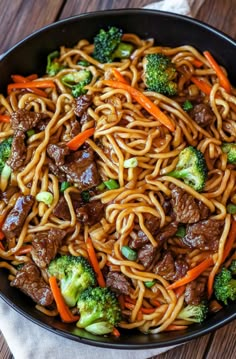 beef and broccoli lo mein noodles in a black bowl on a wooden table