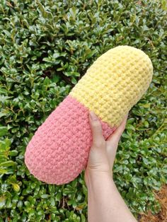 someone is holding up a crocheted slipper in front of some shrubbery