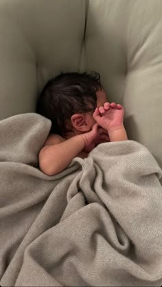 a baby wrapped in a blanket sleeping on a couch