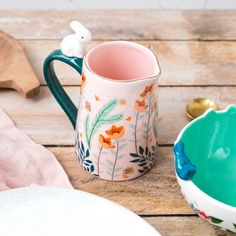 a ceramic mug with flowers on it next to a plate and spoon, sitting on a wooden table