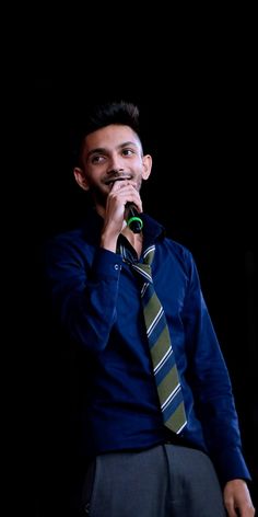 a man wearing a tie and holding a microphone to his mouth while standing in front of a dark background