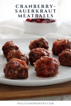 cranberry - sauerkraut meatballs on a white plate with a bowl of cranberries in the background