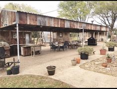 an outdoor patio with potted plants and wooden buildings in the background, surrounded by trees