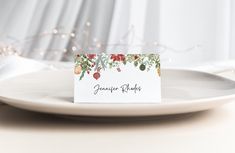 a white plate topped with a place card on top of a table next to christmas lights