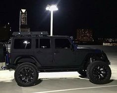 a black jeep parked in a parking lot at night with its lights on and the roof down