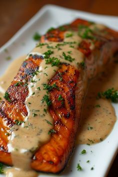 grilled salmon covered in gravy and garnished with parsley on a white plate