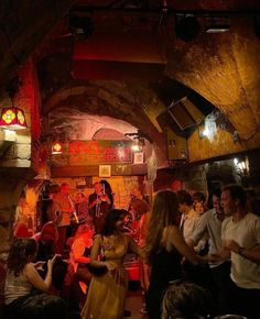 a group of people standing around in a room with red lights on the ceiling and one woman wearing a yellow dress