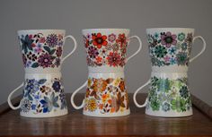 three coffee mugs sitting on top of a wooden table with flowers painted on them