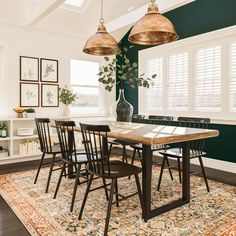 a dining room with green walls and wooden table surrounded by chairs, potted plant on rug