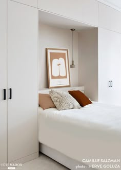 a white bed sitting in a bedroom next to a wall mounted art above it's headboard