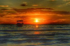 the sun is setting over the ocean with a small boat in the water below it