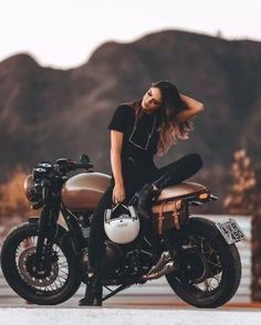 a woman sitting on top of a motorcycle in front of mountains and water with her hair blowing back