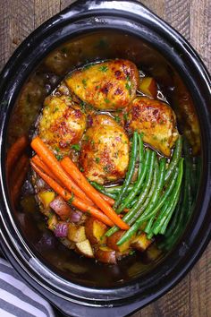 a crock pot filled with chicken, potatoes and carrots on top of a wooden table