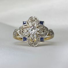 an antique diamond and sapphire ring on a white background, with the center stone surrounded by smaller diamonds