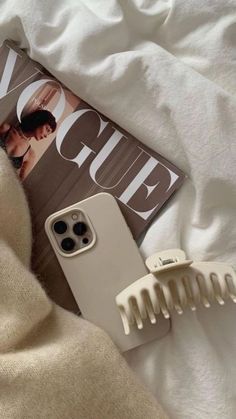 an iphone case sitting on top of a bed next to a hair comb and magazine