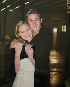 a man and woman hugging each other in front of a building with lights on the ceiling