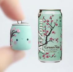 a hand holding a can with a keychain shaped like a tree and a tea bag hanging from it's side