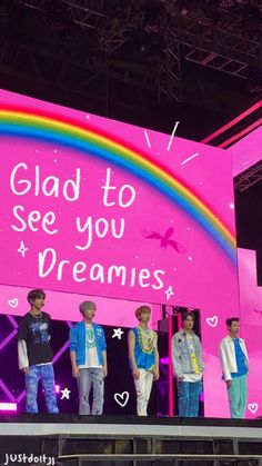 a group of young men standing on top of a stage next to a rainbow sign