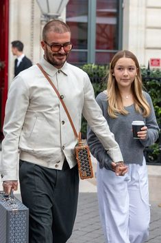 a man and woman are walking down the street with their suitcases, one carrying a coffee cup