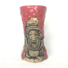 a red and black vase with a face painted on the side, sitting against a white background