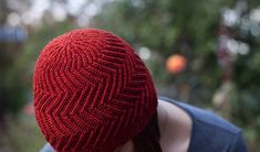 a woman wearing a red knitted hat looking down at her face with trees in the background