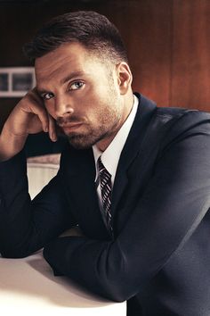 a man in a suit sitting at a table with his hand on his chin and looking off to the side