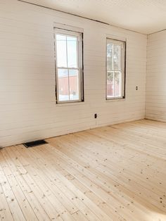 an empty room with wood floors and two windows