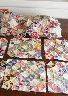 several pieces of quilt laid out on a wooden table with white wall in the background