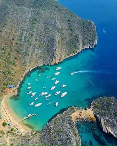 an aerial view of boats anchored in the water near a rocky cliff and shore line