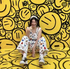 a woman sitting on the ground in front of a wall with smiley faces painted on it