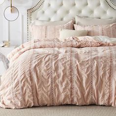 a bed with pink comforter and pillows on top of it in front of a white headboard