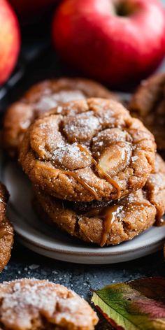 several cookies are stacked on top of each other with apples in the background and leaves around them