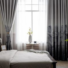 a bed sitting under a large window next to a white vase filled with flowers on top of a table