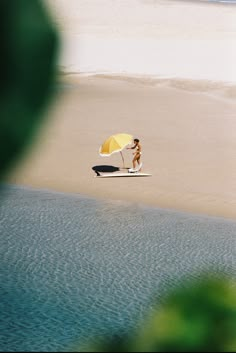 a woman sitting on top of a surfboard next to a yellow and white umbrella