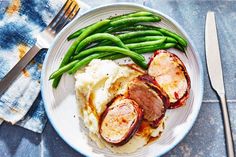 a white plate topped with mashed potatoes and green beans next to fork and knife