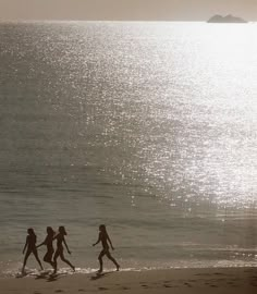 three people are walking along the beach with their surfboards in hand as the sun shines on the water