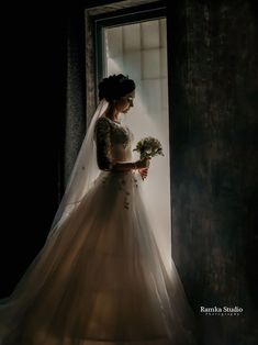 a woman in a wedding dress standing by a window