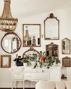 a white dresser topped with lots of mirrors next to a wall filled with framed pictures