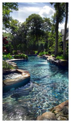 an outdoor swimming pool surrounded by trees and water features clear blue waters, with rocks in the foreground