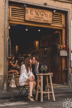 a man and woman are kissing in front of a restaurant with people sitting at tables