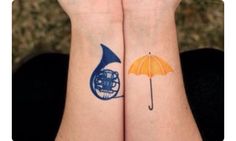 two people with matching tattoos on their arms holding an umbrella and a trumpet in front of them