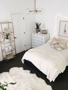 a bedroom with white walls and black flooring is pictured in this image, there are plants on the nightstands next to the bed