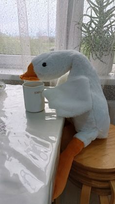 a stuffed duck sitting on top of a wooden stool next to a cup filled with food