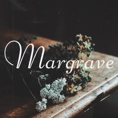 the word margrave is written on a wooden table with flowers and leaves in front of it