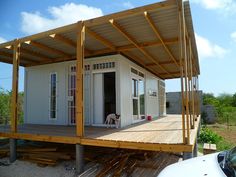 a small white house sitting on top of a wooden deck next to a parked car