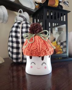 a knitted pumpkin hat sitting on top of a wooden table next to a lantern