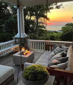 a porch with a swing, couch and fire pit on it at sunset or dawn